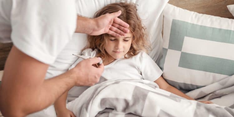 Vater hält seiner im Bett liegenden Tochter die Hand an die Stirn, um zu prüfen, ob diese Fieber hat.