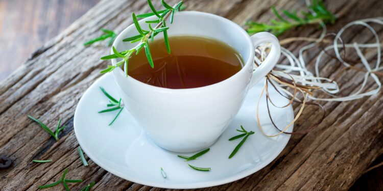 Weiße Tasse mit Kräutertee und einem Rosmarinzweig garniert