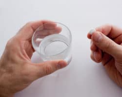 Eine Hand hält ein Wasserglas, die andere eine Tablette