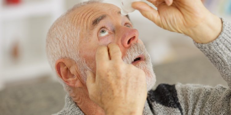 Ein älterer Mann tropft sich Augentropfen ins Auge.