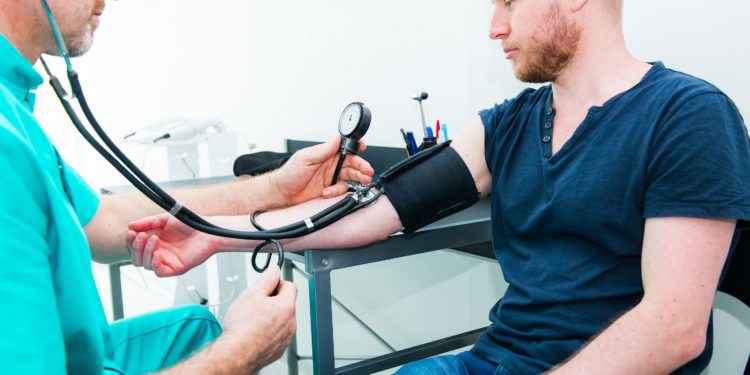 Ein Arzt misst den Blutdruck bei einem jungen Mann.