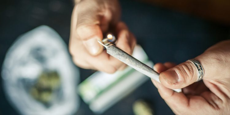 Eine Hand mit einem Feuerzeug zündet einen Joint an