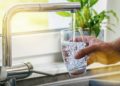 Ein Mann befüllt am Wasserhahn i der Küche ein Glas mit Leitungswasser.
