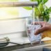 Ein Mann befüllt am Wasserhahn i der Küche ein Glas mit Leitungswasser.