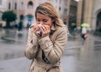 Frau putzt sich bei nasskaltem Wetter die Nase