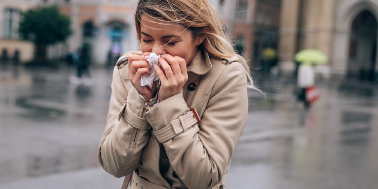 Frau putzt sich bei nasskaltem Wetter die Nase