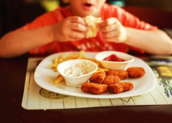 Kind sitzt vor einem Teller mit Fast Food.