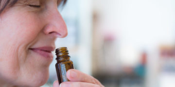 Frau riecht an einem geöffneten Glasfläschchen.