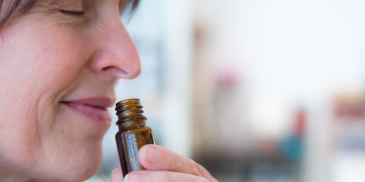 Frau riecht an einem geöffneten Glasfläschchen.