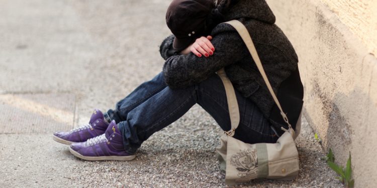 Junges Mädchen sitzt auf dem Boden und hat ihren Kopf in ihre verschränkten Arme gelegt