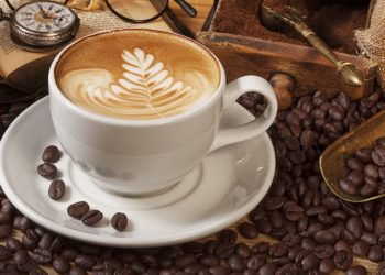 Eine Tasse Kaffee steht auf einem Tisch und ist von Kaffeebohnen umgeben.