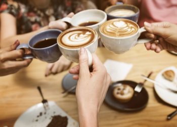 Vier Hände halten jeweils eine Kaffeetasse und stoßen damit an