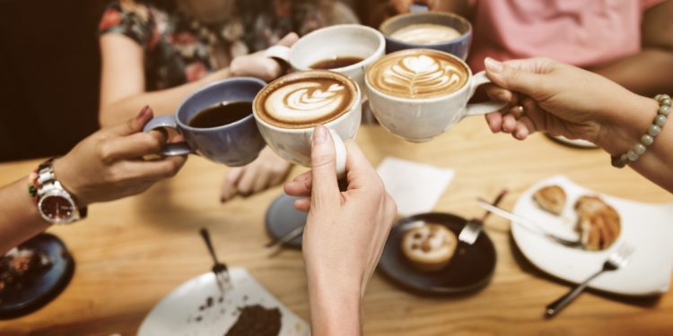 Vier Hände halten jeweils eine Kaffeetasse und stoßen damit an