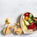 Herzfömige Schale gefüllt mit Obst und Gemüse. Links daneben ein Spielzeug Holzfahrrad.