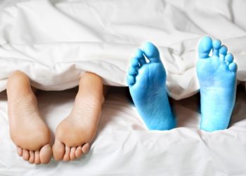 Zwei paar Füße gucken unter der Decke hervor, eines davon blau gefroren.