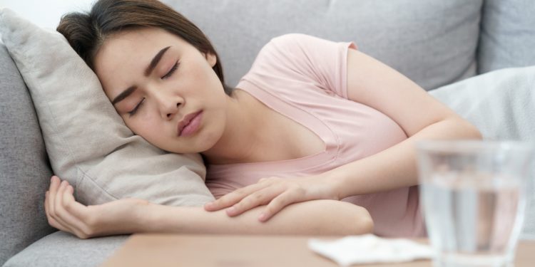 Eien Frau liegt zugedeckt auf dem Sofa und schläft. 