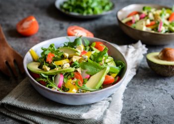 Drei Teller mit gemischtem Salat und eine aufgeschnittene Avocado und Tomate daneben