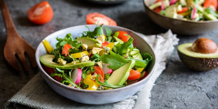 Drei Teller mit gemischtem Salat und eine aufgeschnittene Avocado und Tomate daneben