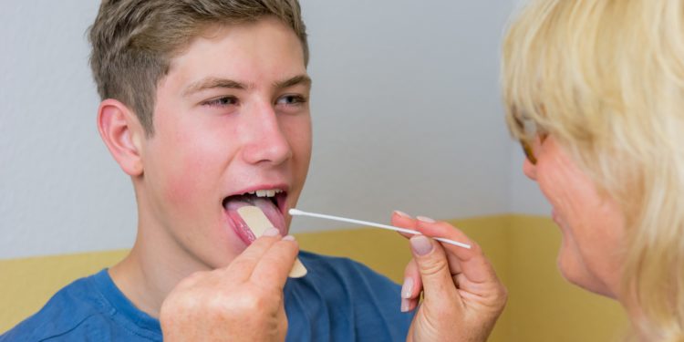 Eine Ärztin macht einen Abstrich im Mund eines Teenagers.
