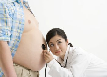 Eine Ärztin untersucht den Bauch eines übergewichtigen Mannes.