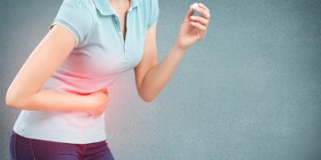 Eine Frau hält sich in einer gekrümmten Körperhaltung eine Hand vor dem Bauch.