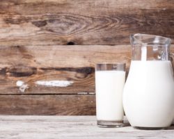 Milch in einem Krug und in einem Glas auf einem alten Tisch