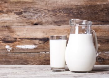 Milch in einem Krug und in einem Glas auf einem alten Tisch