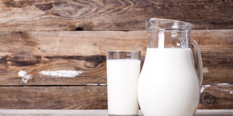 Milch in einem Krug und in einem Glas auf einem alten Tisch