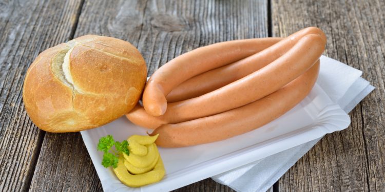 Zwei Paar Wiener Würstchen mit scharfem Senf und einem Brötchen auf einem Pappteller