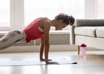 Eine Frau in Sportkleidung macht zu Hause Liegestütze auf einer Matte.