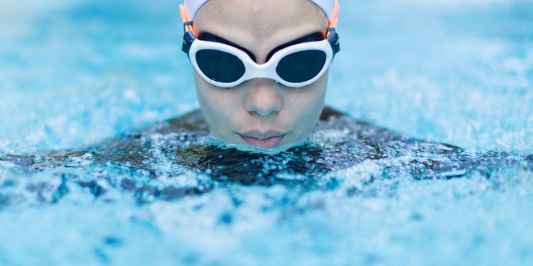 Eine Frau mit Schwimmbrille und Schwimmkappe beim Brustschwimmen.