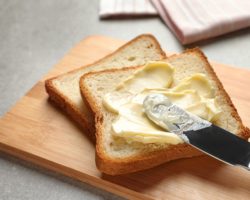 Toast liegt auf einem Brettchen und wird mit Margarine bestrichen.