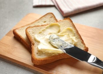 Toast liegt auf einem Brettchen und wird mit Margarine bestrichen.