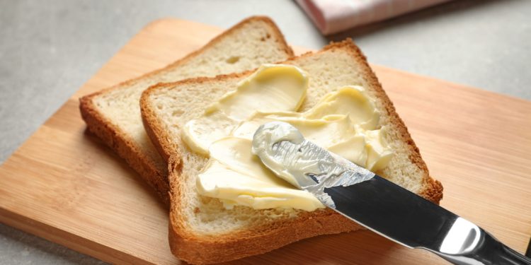 Toast liegt auf einem Brettchen und wird mit Margarine bestrichen.