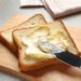 Toast liegt auf einem Brettchen und wird mit Margarine bestrichen.