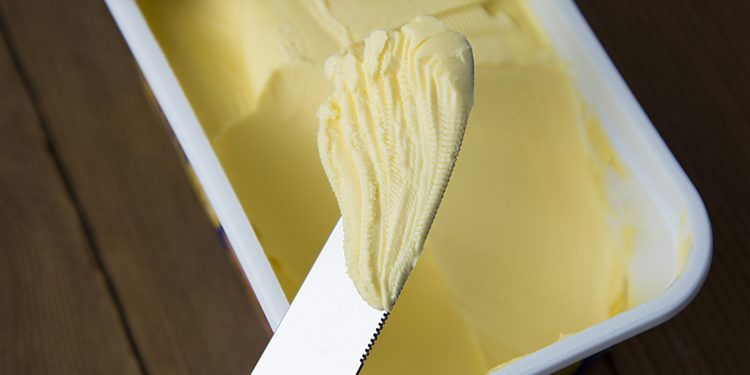 Margarine in einem Kunstoffbecher und ein Messer, mit welchem etwas davon entnommen wurde.