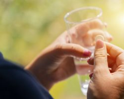 Eine Frau hält in einer Hand eine Tablette und in der anderen ein Glas Wasser