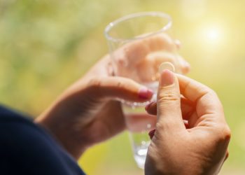 Eine Frau hält in einer Hand eine Tablette und in der anderen ein Glas Wasser