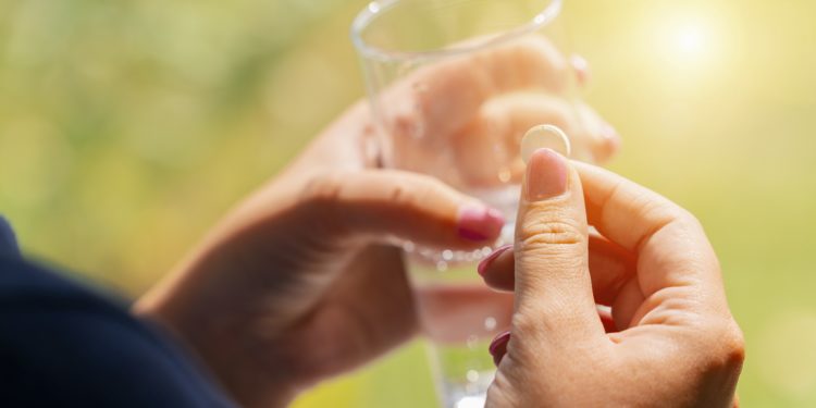 Eine Frau hält in einer Hand eine Tablette und in der anderen ein Glas Wasser