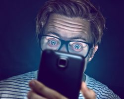 Ein Mann mit Brille starrt mit großen Augen auf ein Smartphone.