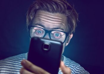 Ein Mann mit Brille starrt mit großen Augen auf ein Smartphone.