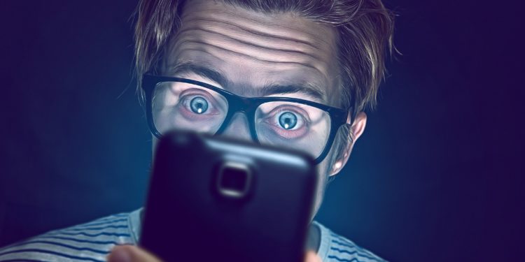 Ein Mann mit Brille starrt mit großen Augen auf ein Smartphone.