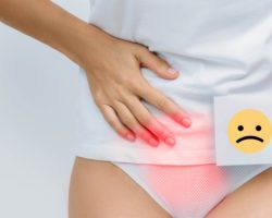 Frau hält sich vor Schmerzen mit der rechten Hand den Unterbauch und hält in der linken Hand einen Zettel mit einem traurigen Smiley