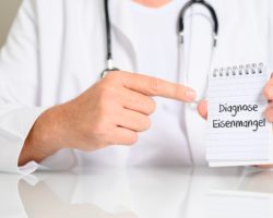 Arzt hält einen Schriftblock mit dem Text "Diagnose Eisenmangel" in die Kamera