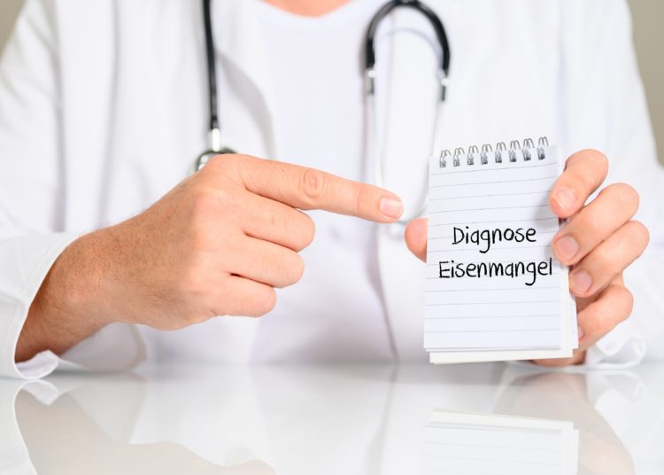 Arzt hält einen Schriftblock mit dem Text "Diagnose Eisenmangel" in die Kamera