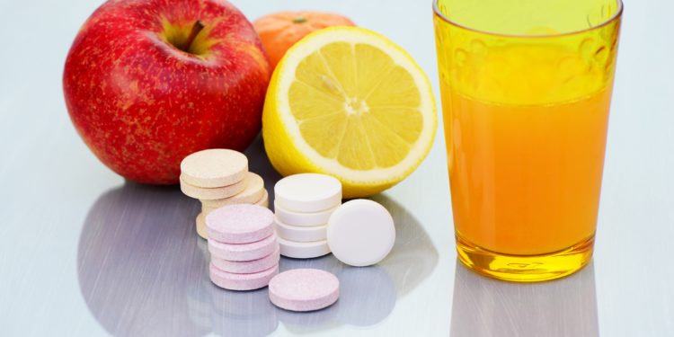 Zwei Äpfel, eine halbe Zitrone, einige Vitamintabletten und ein Glas Orangensaft