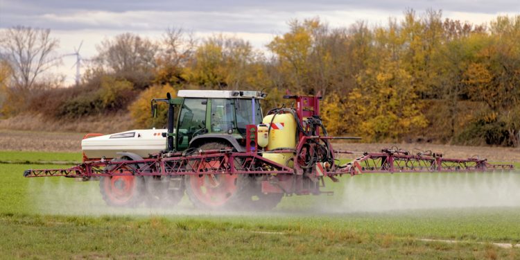 Traktor mit Feldspritze beim Ausbringen von Pflanzenschutzmittel