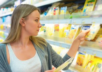 Eine Frau nimmt sich eine Käse-Packung aus einem Regel in einem Supermarkt.