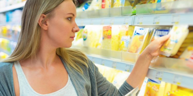 Eine Frau nimmt sich eine Käse-Packung aus einem Regel in einem Supermarkt.