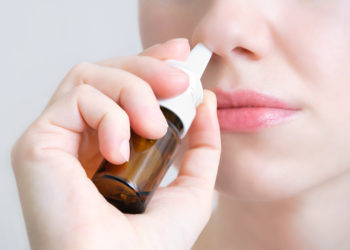 Junge Frau sprüht Nasenspray in ihre Nase